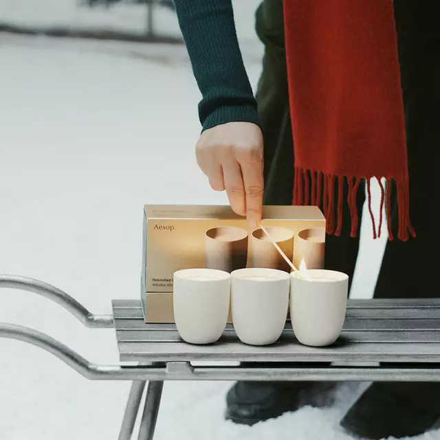 A hand lights a candle in an Aesop gift set.