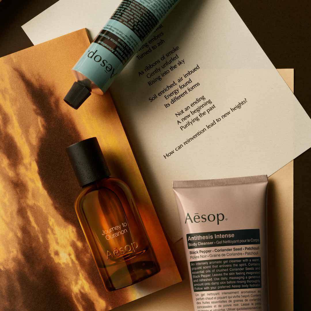 Aesop Journey to Ouranon bottle with pump bottle and tube arranged on papers with a glowing landscape image.