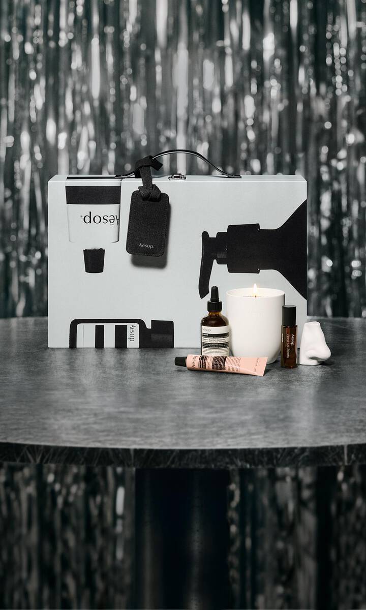 Aesop gift set and skincare products arranged on a table against a festive, softly lit backdrop.