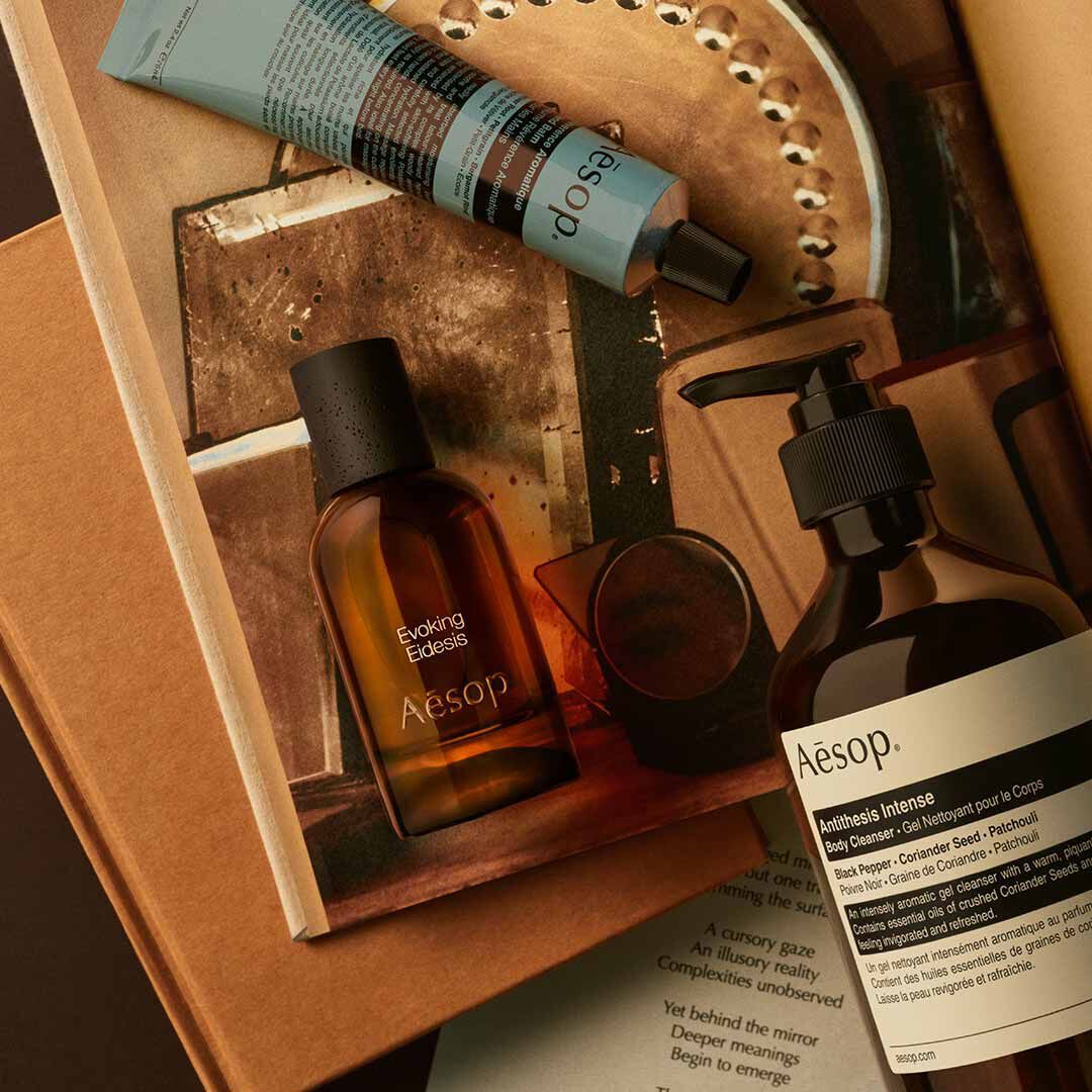 Aesop Evoking Eidesis bottle with pump bottle and blue tube arranged on papers and mirrored tray imagery.
