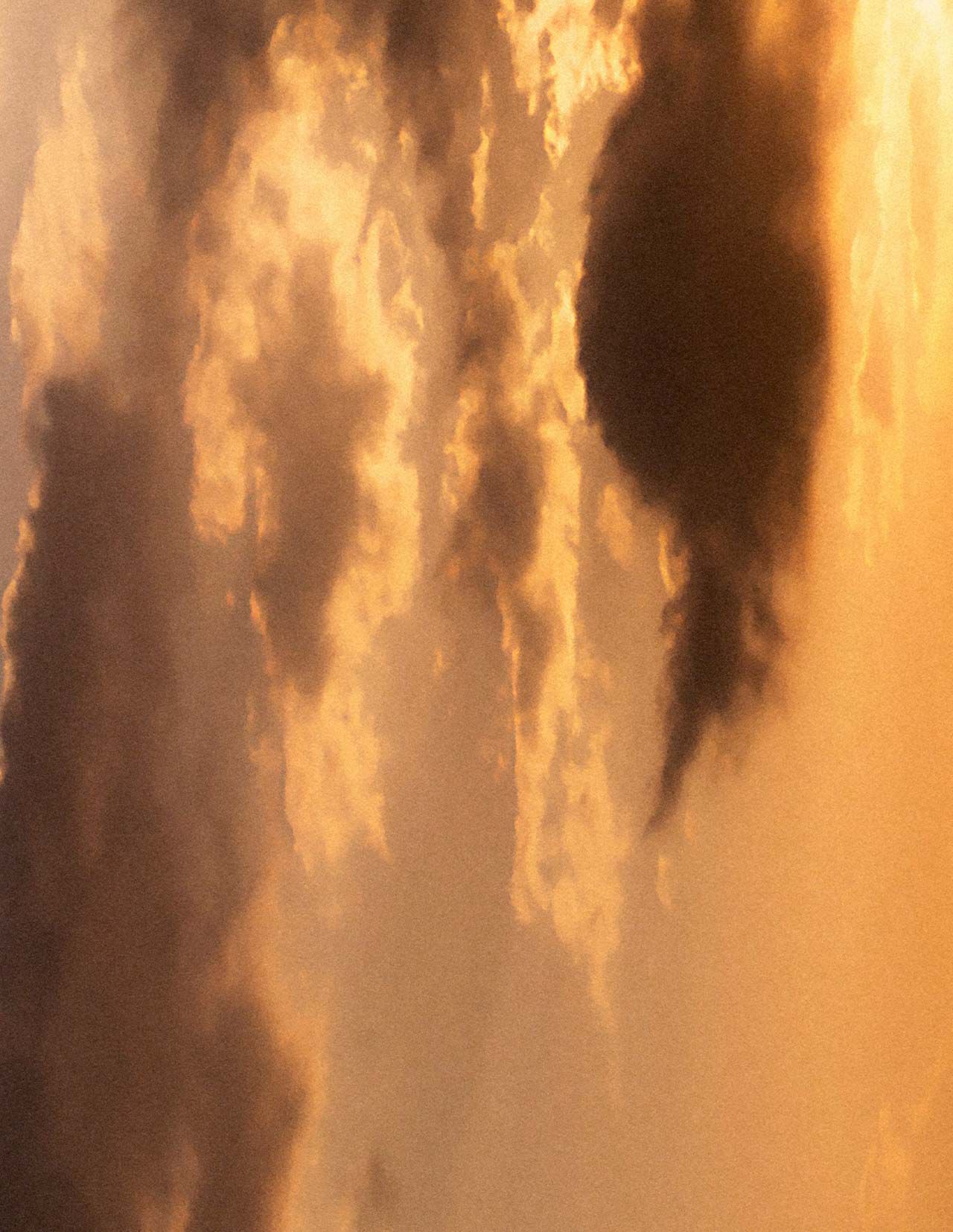 Golden sunset sky with layered clouds in warm amber tones, soft diffused light, and darker cloud forms crossing the scene.