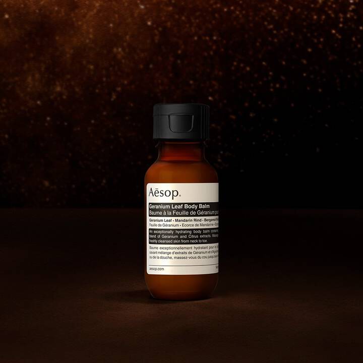 An Aesop Geranium Leaf body balm bottle against a dark, textured background.