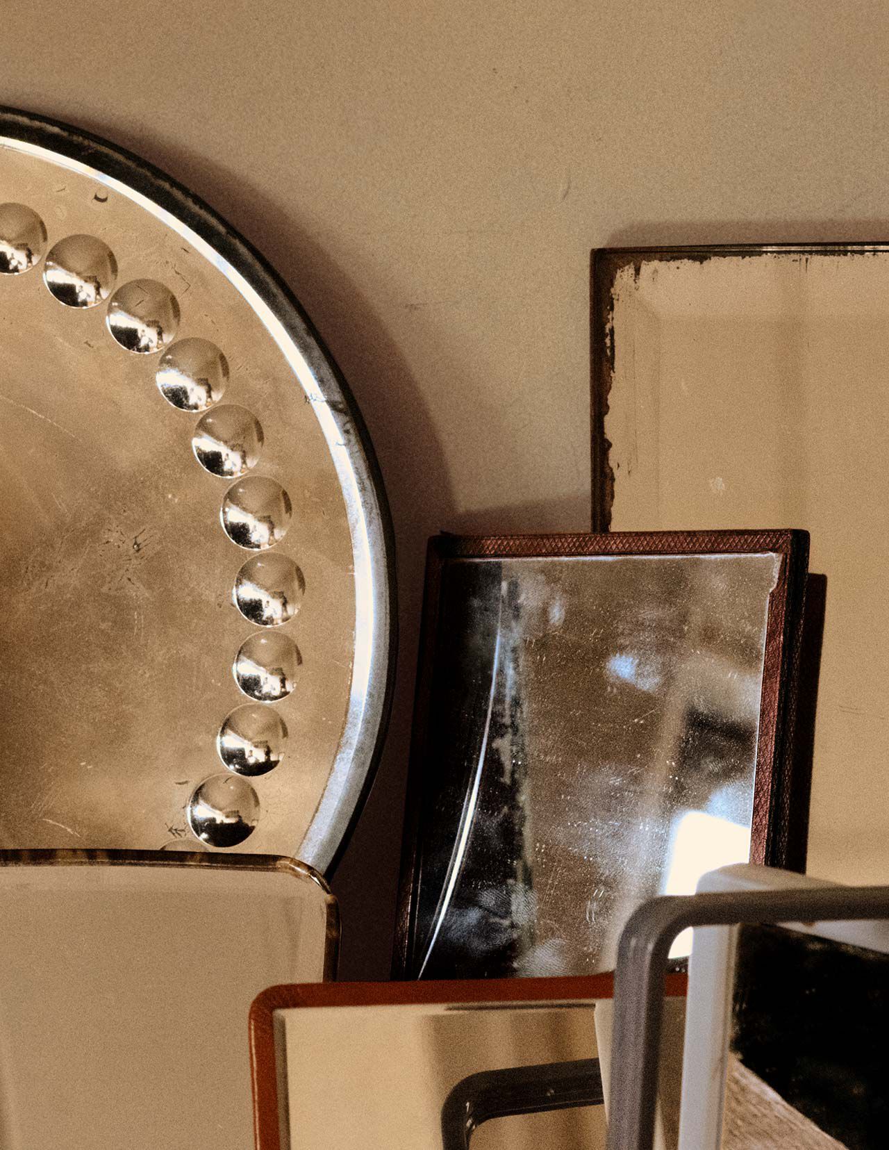 Stacked metallic and stone objects in bronze, beige and dark brown tones, arranged as overlapping geometric forms against a neutral wall.
