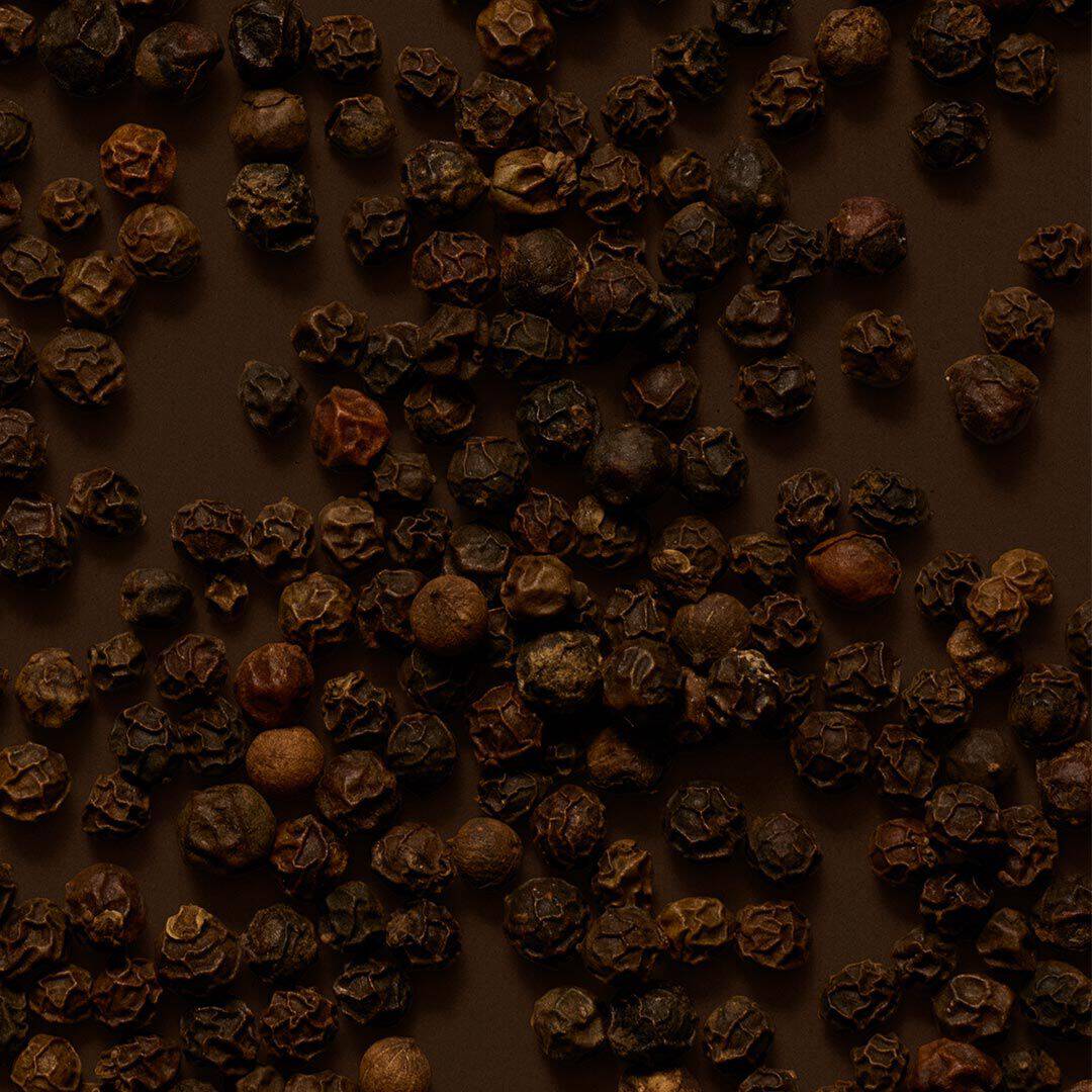Close-up of peppercorns scattered across a dark brown surface.