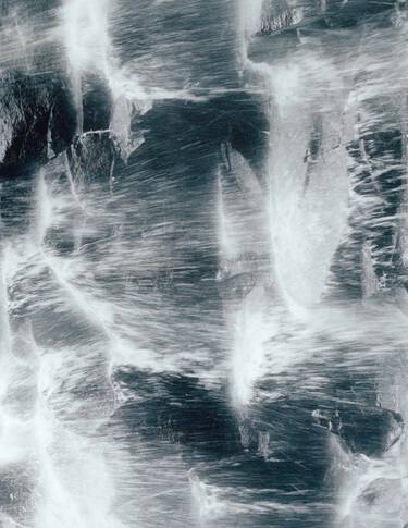 Dark blue-grey rock surface with white vein-like streaks and rough mineral texture, forming a high-contrast marbled pattern.
