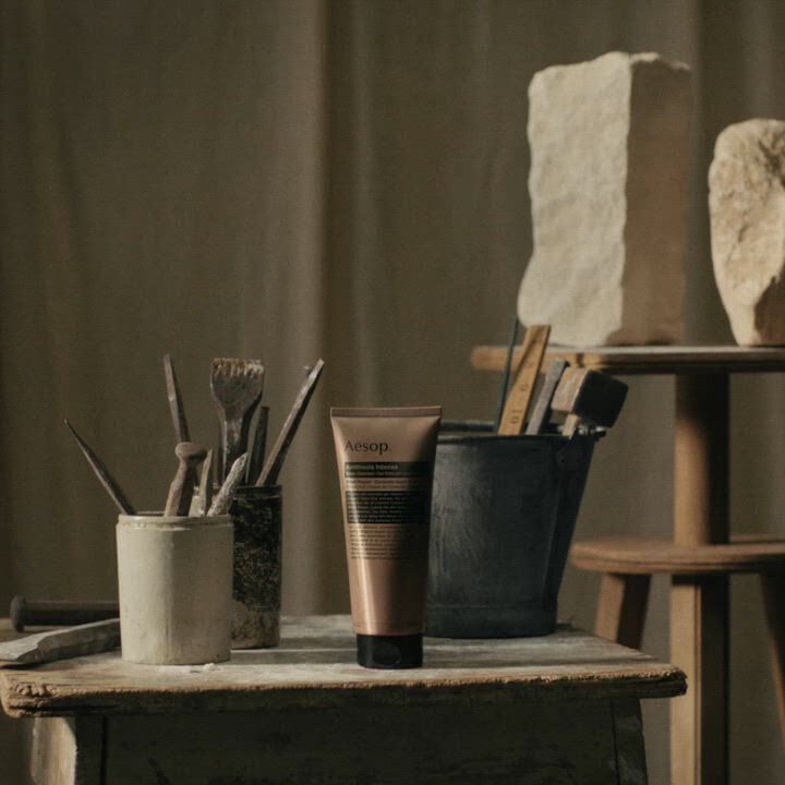 Aesop Antithesis Intense Body Cleanser tube on a work table with brushes and stone sculptures.